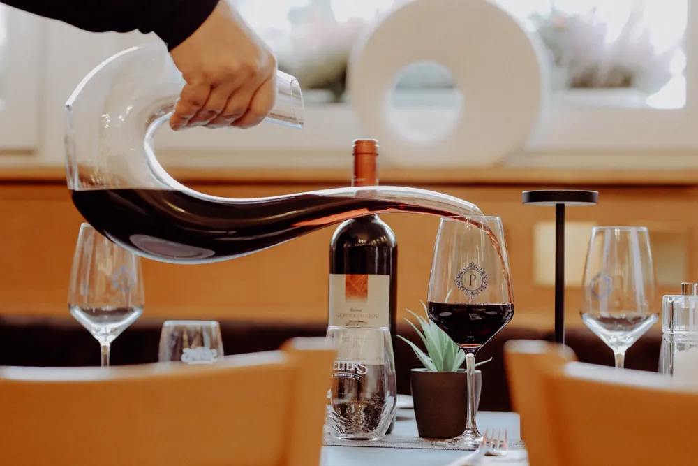 Rotwein wird am gedeckten Tisch aus einer Karaffe eingeschenkt